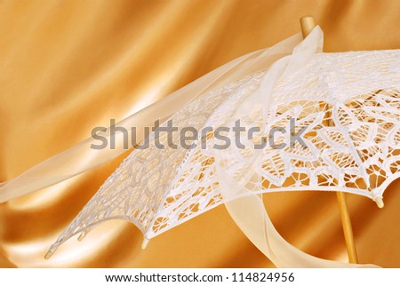 Beautiful lace parasol with chiffon ribbon on gold satin background with copy space.  Close-up with shallow dof.  Ideal for use as a bridal shower invitation.