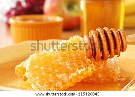 Sunlit still life of golden honeycombs with fresh honey and drizzler.  Jars of honey and fresh fruit in background.  Closeup with shallow dof.