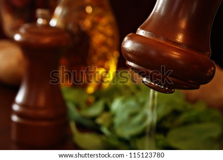 Artistic, low key still life of wooden salt shaker with pepper mill, salad ingredients, and dressing in background.  Macro with extremely shallow dof.  Motion blur on salt captured with long exposure.