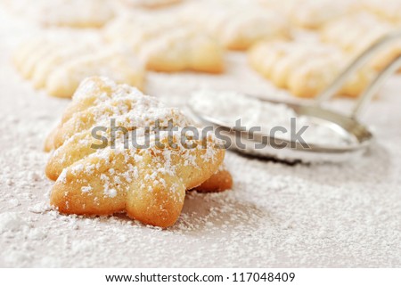 Freshly baked Christmas tree cookies sprinkled with confectioners sugar on parchment paper.  Stainless steel sugar duster in soft focus in background.  Macro with extremely shallow dof.