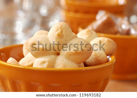 Freshly baked sugar cookies (spritz cookies made with cookie press) in gold dessert dish with caramel candies in background.  Macro with extremely shallow dof.