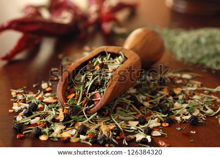 Still life of herbs and spices spilling from small wooden scoop onto wood cutting board with peppers in background.  Macro with shallow dof.  Selective focus on front edge of scoop.