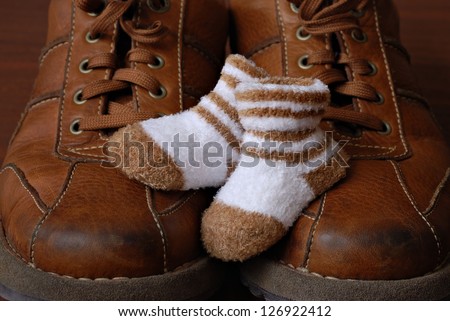 Baby booties nestled on top of parent's well worn leather shoes. Macro with shallow dof.