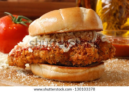 Chicken parmesan sandwich (seasoned and fried chicken breast with tomato basil marinara sauce and mozzarella on a grilled bun) with ingredients and cooking oil in background.  Macro with shallow dof.