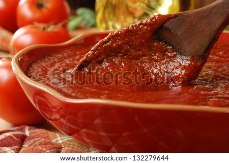 Freshly prepared pasta or pizza sauce in bowl with wooden spoon.  Tomatoes, olive oil, and herbs in background.  Closeup with shallow dof.  Selective focus on sauce in spoon.