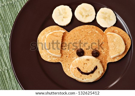 Fun kid\'s breakfast of a smiling monkey face with chocolate chips for eyes on plate with banana slices.