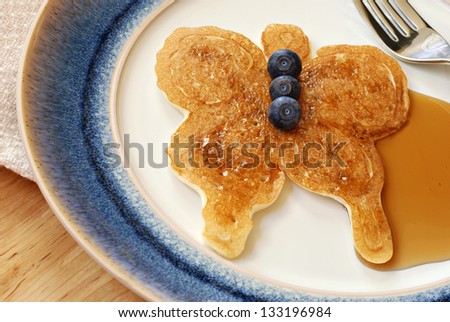 Fun butterfly shaped pancake with fresh blueberries and syrup on decorative plate.  Macro with shallow dof.