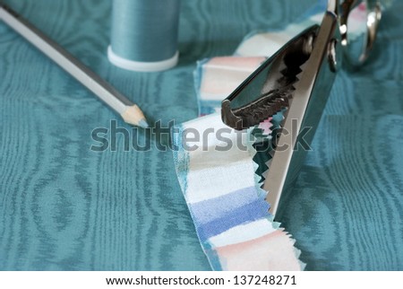 Pinking shears with strip of fabric showing detail of cut edge.  Moire fabric, thread and marking pencil in background.  Macro with extremely shallow dof.