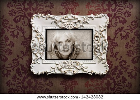 Elegant wooden frame with sepia toned casual portrait of happy mature woman on Victorian style wallpaper.