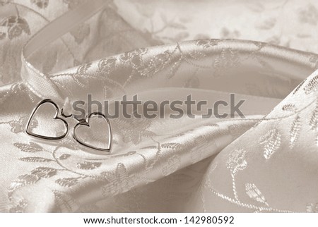 Wedding background of two silver hearts joined together with ribbon on elegant satin brocade fabric. Sepia toned macro with extremely shallow dof.