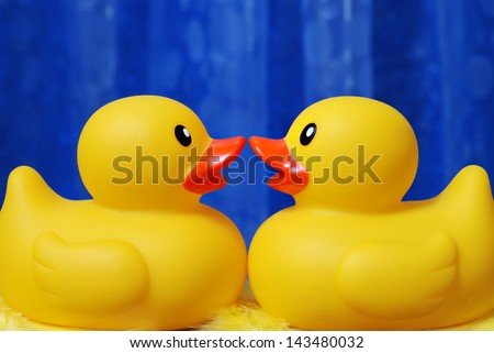 Rubber duck couple sharing a kiss with blue shower curtain is soft focus as background.  Macro with shallow dof.