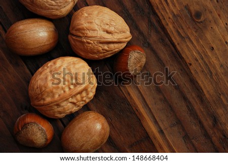 Assorted whole nuts (walnuts, hazelnuts, pecans) on rustic dark wood background.  Low key still life with directional natural lighting for effect.