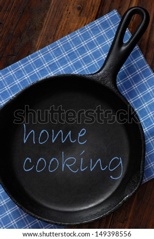 Home cooking concept with text added to still life of vintage cast iron skillet on rustic background.  Ideal for use as menu design or cookbook cover.