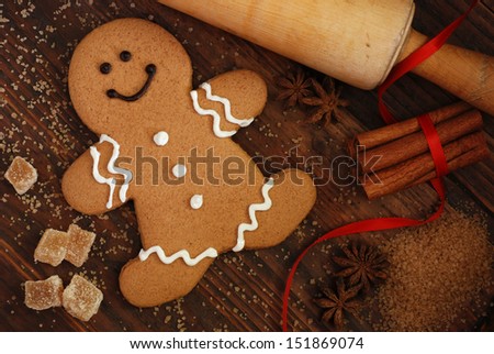 Smiling gingerbread man with sugar, spices, and vintage rolling pin on rustic, dark wood background.  Low key still life with directional, natural lighting for effect.