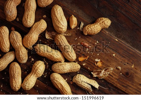 Roasted peanuts with broken shells and pieces scattered on rustic, dark wood background.  Low key still life with directional, natural lighting for effect.