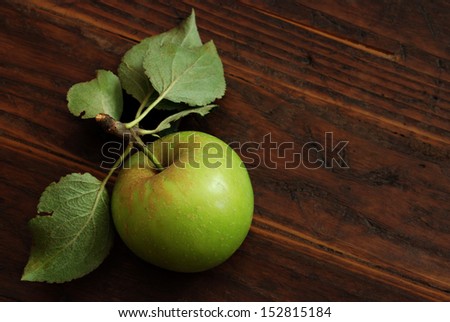 Green apple with leaves and stem on rustic dark wood background.  Low key still life with directional, natural lighting for effect.