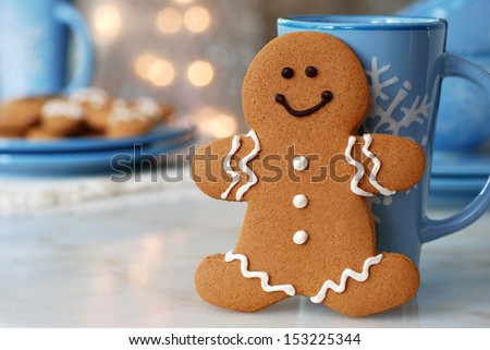 Smiling Gingerbread Man Standing Next To Snowflake Mug. Plate Of Additional Cookies And Defocused Holiday Lights In Background. Closeup With Shallow Dof. Copy Space Included For Text.