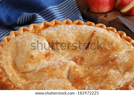 Freshly baked apple pie with sliced apple and knife on wooden cutting board in background.  Rustic still life with natural, directional lighting and shallow dof.