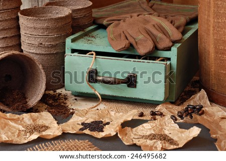 Rustic gardening still life with assorted seeds, organic starter pots, work gloves and vintage wooden box.  Selective focus on drawer with twine.