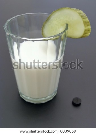 Glass of milk with piece of cucumber and 	activated carbon near it