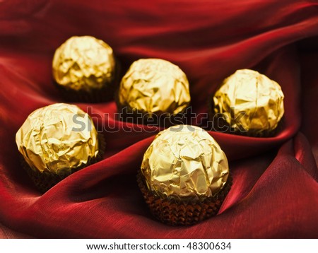 confection in golden candy wrapper at dark red textile