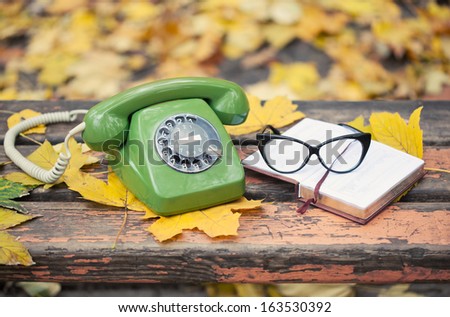 green vintage phone, book and glasses on bench in autumn park