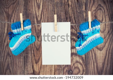 knitted baby socks and blank note hanging on clothesline against wooden background