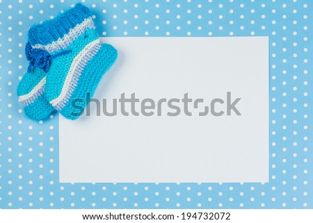 knitted baby socks and blank note on blue polka dot background