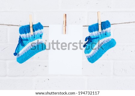 knitted baby socks and blank note hanging on clothesline against white brick wall