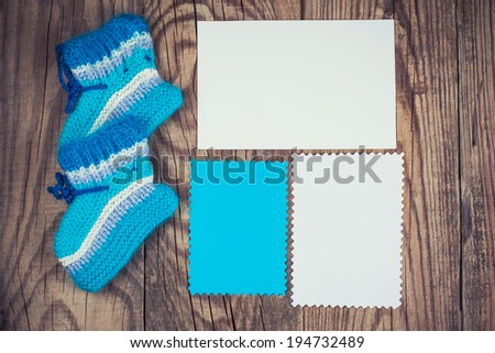 knitted baby socks and blank note on wooden background