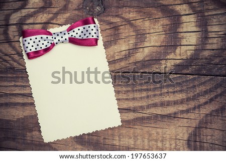 blank paper sheet with pink and white polka dot bow on wooden background