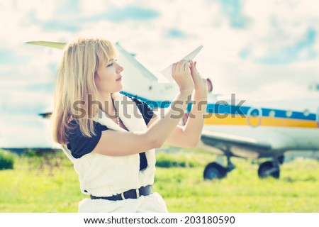 beautiful woman holding paper plane against real plane