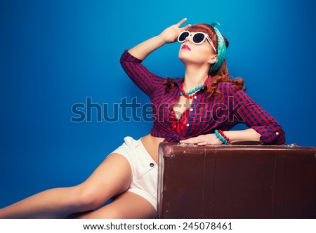 beautiful pin-up girl posing with vintage suitcase against blue background