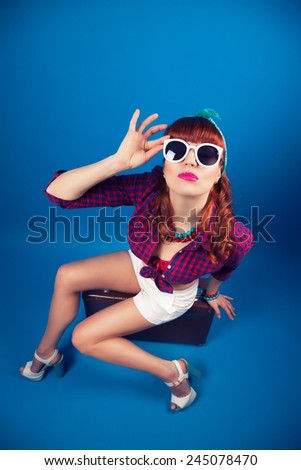 beautiful pin-up girl posing with vintage suitcase against blue background