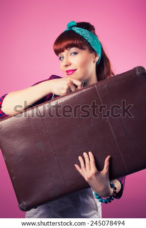 beautiful pin-up girl posing with vintage suitcase against pink background