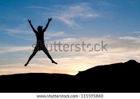 Star jump for joy at sunset. Young woman in the air as a silhouette figure.
