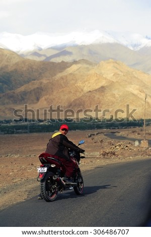 LEH, INDIA. JUNE 13, 2012 :Tibetan monk riding the motorbike on high altitude Ladakh-Leh road in himalayan mountain, state of Jammu and kashmir, India