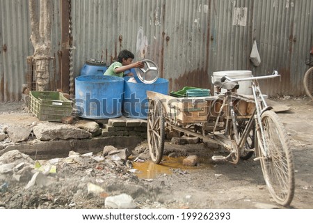 NEW DELHI, INDIA - MARCH 10: Unidentified Indian boy washes dishes on his own tricycle on March 10, 2014 in Delhi, India. Street dishwashers in demand among Indian fast-food restaurants.