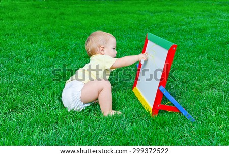 Beautiful little baby  draws sitting on a lawn