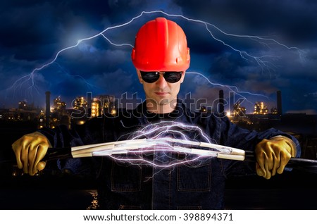 Electrician keeps cables that shoot lightning on the background of industrial landscape and sky with lightning