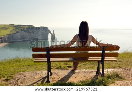 young woman resting on a bench on top of a cliff in Etretat, Normandy, France.