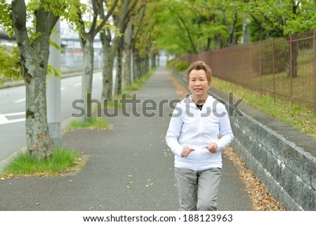 Asian elderly woman that is running the sidewalk there is a forest of the fresh green