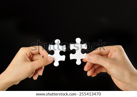 The hands of human beings that have a jigsaw puzzle that was taken with a black background