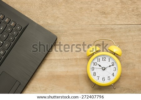 Black notebook  and yellow clock on wooden background.