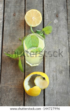 Top view of glass of lemonade with mint leaf in it, with mint twig, half cut lemon and lemon peel on table