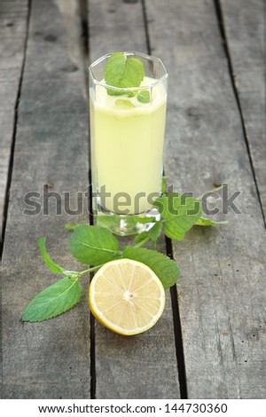 Glass of lemonade with mint and cut lemon on wooden background