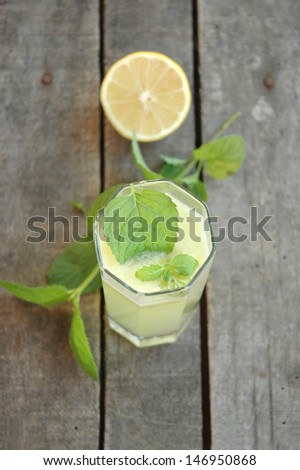 Top view of glass of lemonade with mint leafs in glass, and mint twig on table, with cut lemon half