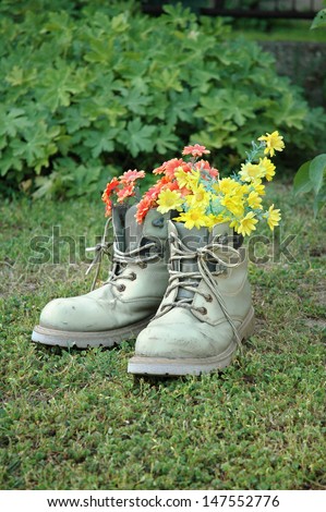 Vertical image of red and yellow flowers in old gray shoes on grass