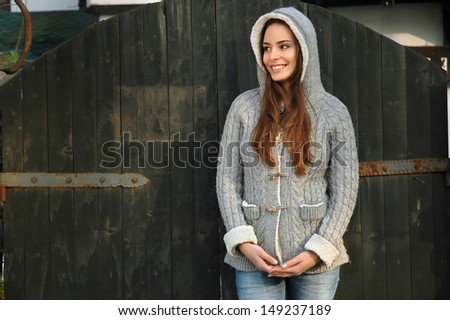 young woman with hood on, in front of old door, smiling innocent and seductive at the same time. Copy space