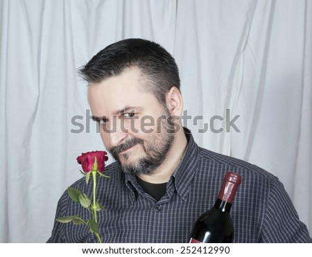Male smelling rose holding bottle of wine, seductive look